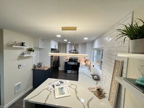 Une cuisine moderne avec des meubles blancs, un îlot central et un luminaire suspendu.