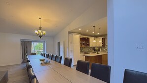 Un comedor moderno con una mesa larga y sillas, un candelabro, y vistas a una zona de cocina.