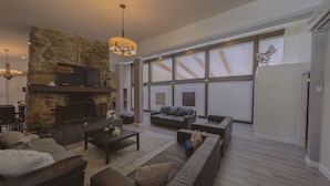 Un salón espacioso con chimenea de piedra, muebles modernos y ventanas amplias.