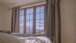 Un dormitorio con un ventanal grande, una cama y cortinas.