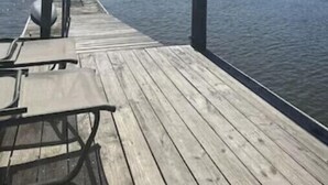 En träbrygga som sträcker sig ut över stilla vatten, med ett avskärmat sittområde och en liten byggnad i bakgrunden.