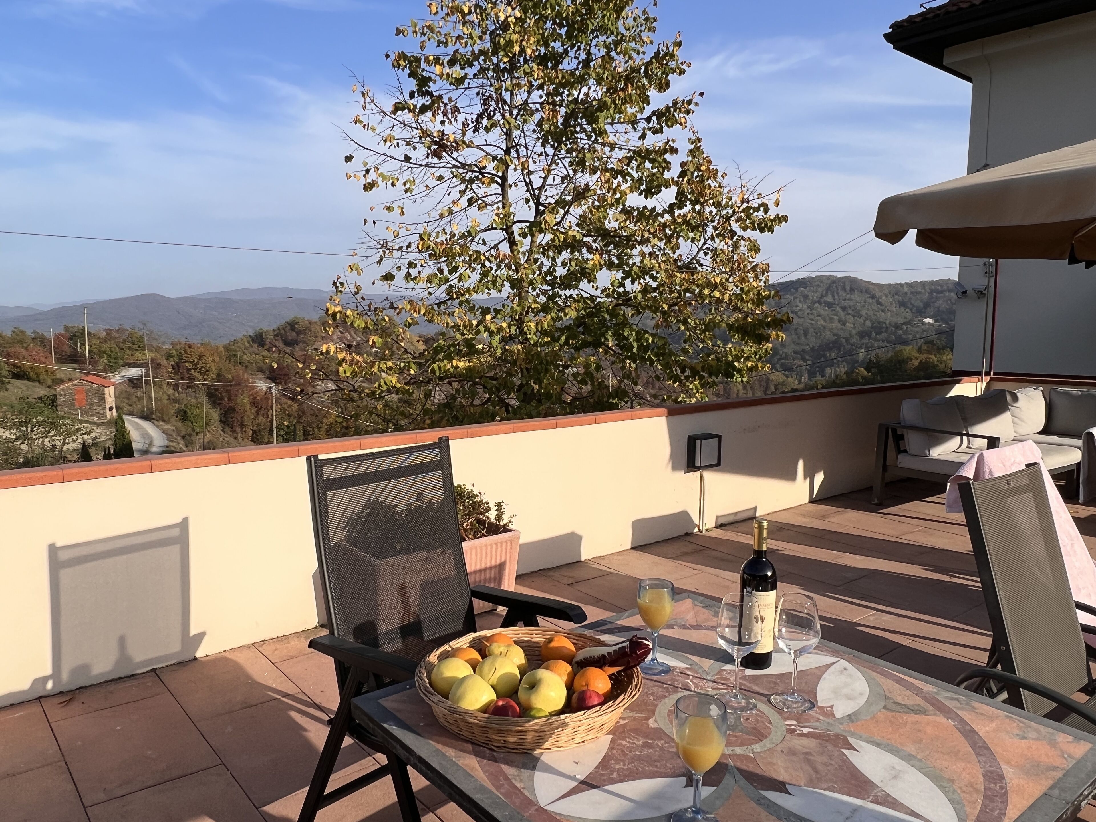 Ein Balkon mit Tisch, gedecktem Geschirr, Obstkorb und einer Weinflasche.