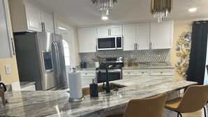 A modern kitchen with white cabinets, stainless steel appliances, a marble island with two bar stools, and a herringbone-patterned backsplash. - Loera’s Inn
Located right off 95 exit Dumfries, 12 minutes from Quantico, VA. (Dumfries)