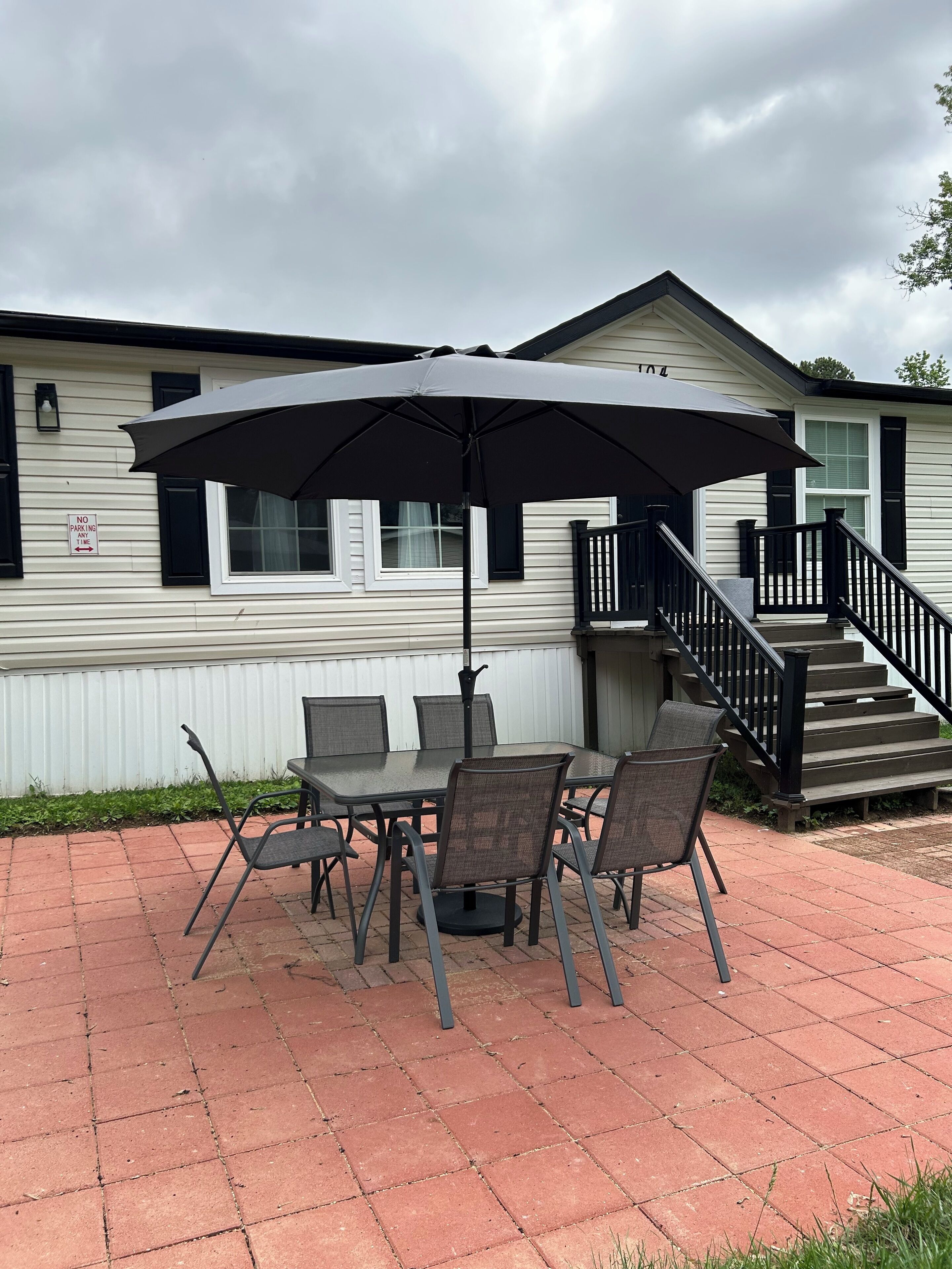 Une terrasse avec une table et des chaises, un grand parasol et un escalier menant à un bâtiment blanc aux bordures noires.