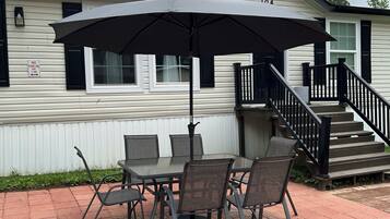 Une terrasse avec une table et des chaises, un grand parasol et un escalier menant à un bâtiment blanc aux bordures noires.