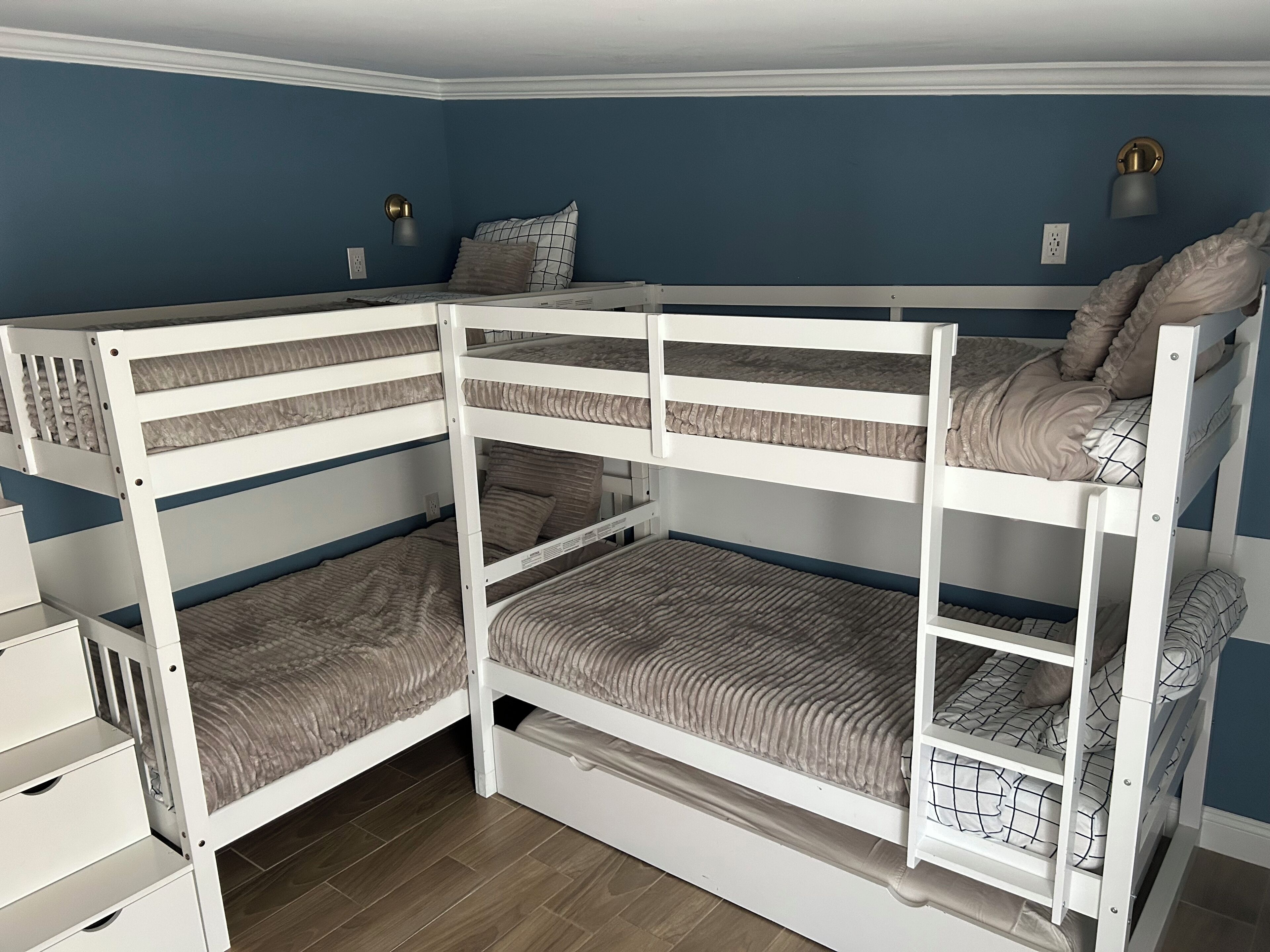 Ein Schlafraum mit Etagenbetten, einer blauen Wand, einer weißen Kommode und einem Nachttisch.