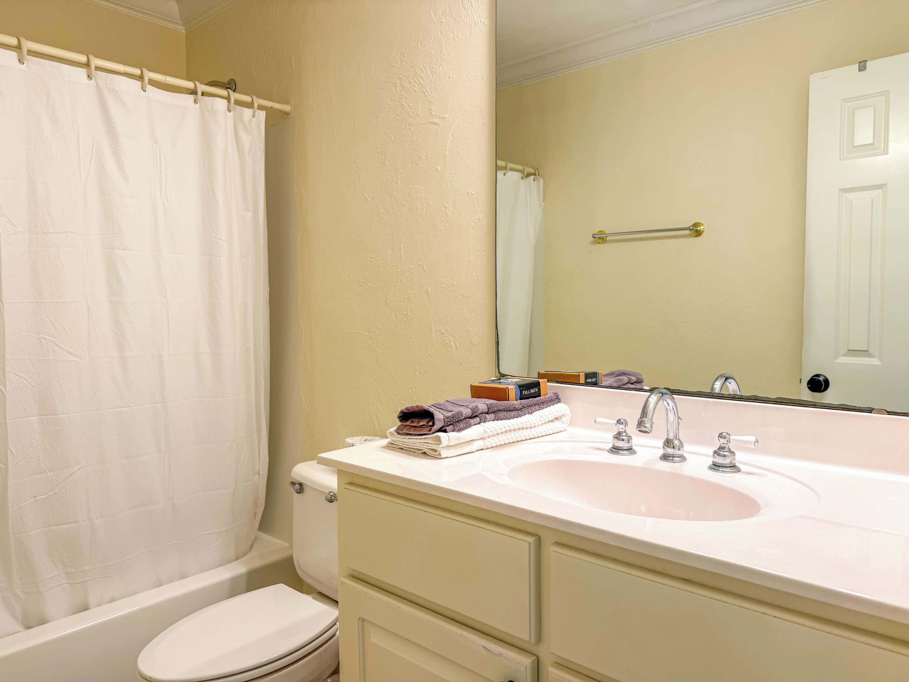 A bathroom with a white toilet, a sink with a mirror, and a shower curtain.