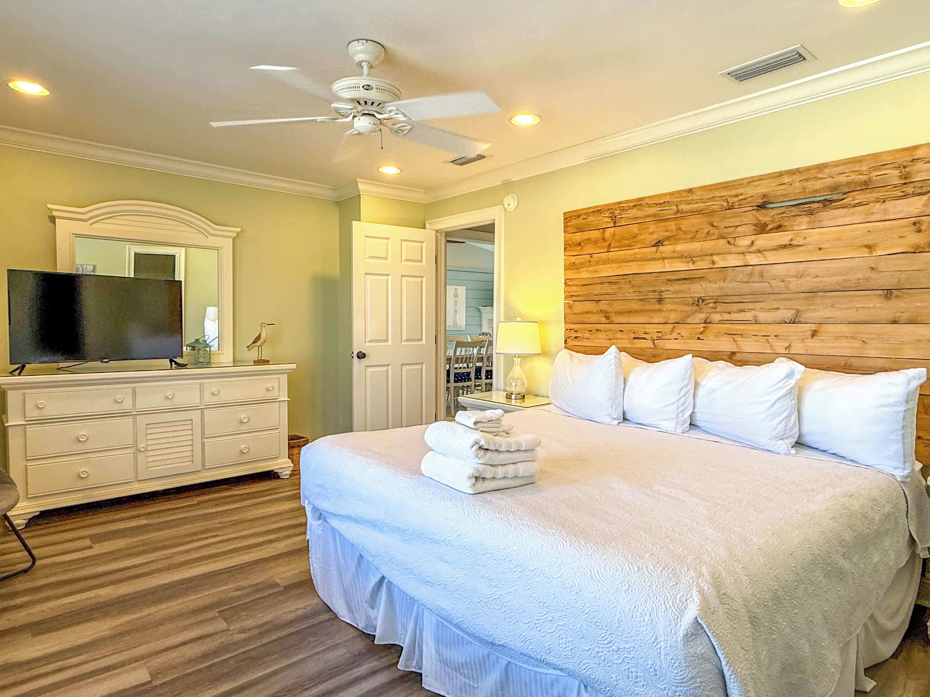 A bedroom with a bed, a dresser, a television, and a ceiling fan.
