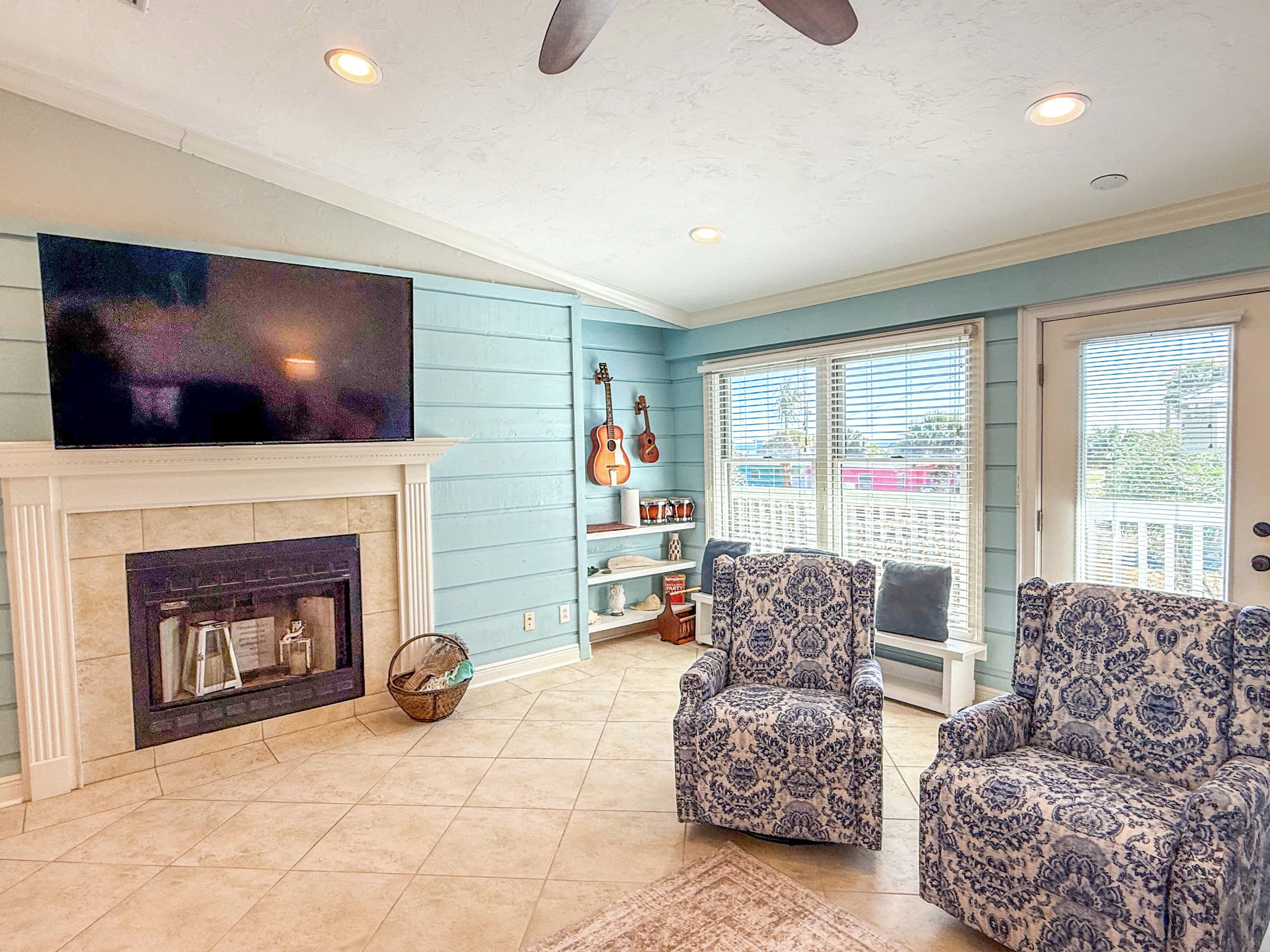 A living room with a fireplace, a television, patterned chairs, and a guitar on the wall.