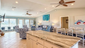 A spacious kitchen with a large island, ceiling fans, and a dining area with white chairs.