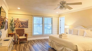 A bedroom with a bed, a ceiling fan, a window with blinds, a chair, and a table.