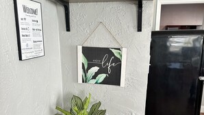 Een keuken met een zwarte koelkast, een houten kast, een bord met de tekst 'Welkom', een bord met 'Happy Home' en een lijst met de tekst 'geniet van het leven'.