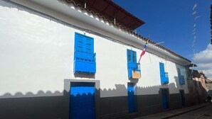 A white building with blue doors and windows, a flag, and a clear sky. - The Sleepy Mouse (Cusco)
