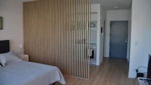 Quarto de hotel com cama, mesa de cabeceira, divisória de madeira, porta e televisão.