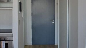 Um corredor com piso de madeira, uma porta fechada e um forno embutido à esquerda.