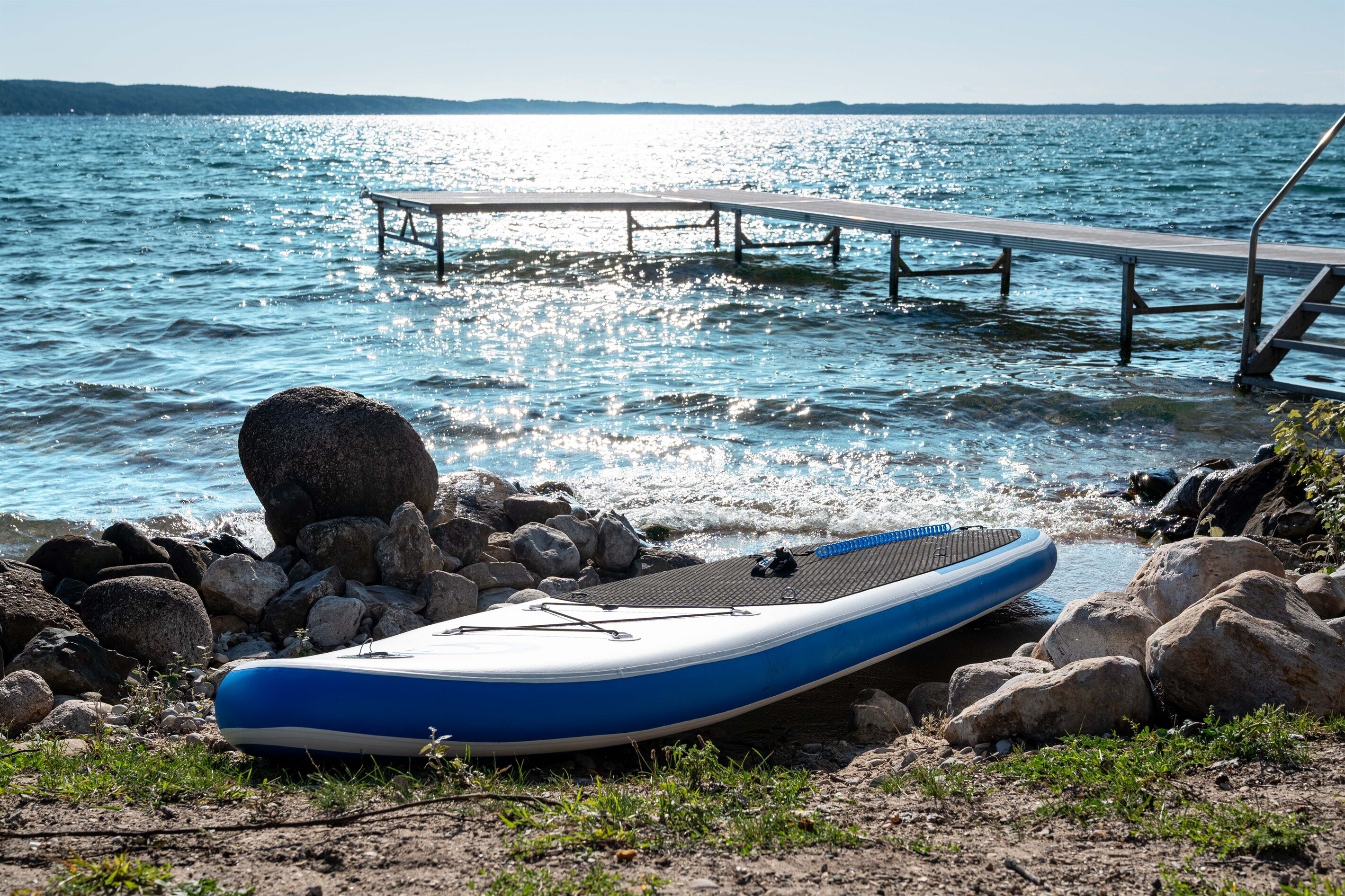Ein blaues Luftboot liegt an einem felsigen Ufer, mit einem Steg, der sich in ruhiges Gewässer erstreckt.