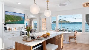A modern kitchen with a large island, a dining area with a view of the water, and a TV mounted on the wall. - Crystal Lake Retreat with hot tub and dock (Beulah)
