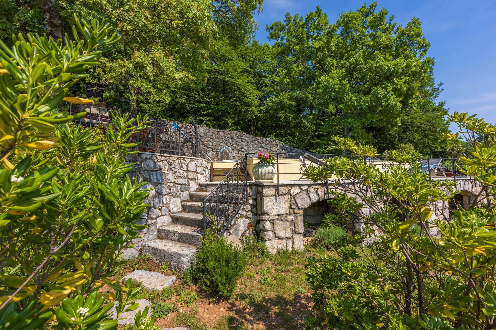 A stone staircase leading to a building with a balcony, surrounded by lush greenery and trees.