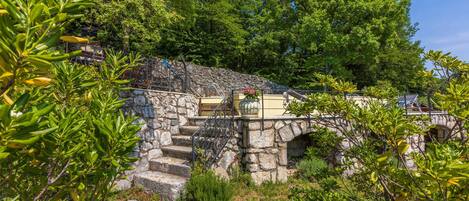 A stone staircase leading to a building with a balcony, surrounded by lush greenery and trees.