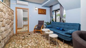 A cozy living area with a stone wall, a blue sofa, a wooden chair, and two small tables. - Holiday home with internet access and air conditioning (Grižane)