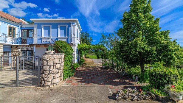 A two-story house with a stone wall entrance, a paved driveway, and a garden with trees and shrubs. - Holiday home with internet access and air conditioning (Grižane)