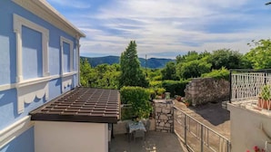 A blue building with a tiled roof, a stone wall, and a small patio with a table and chairs. - Holiday home with internet access and air conditioning (Grižane)