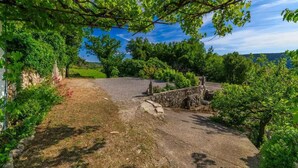 A stone pathway leading to a rustic stone structure in a lush, green garden with a clear sky. - Holiday home with internet access and air conditioning (Grižane)