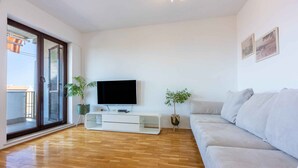 A modern living room with a flat-screen TV, a white sofa, and two potted plants.