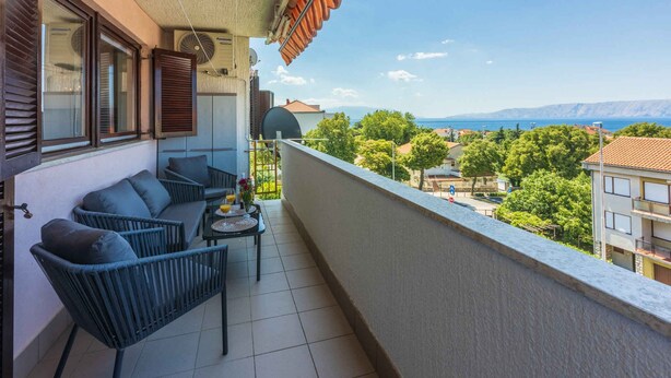 A balcony with a view of the sea, a table with chairs, and a small table with flowers.