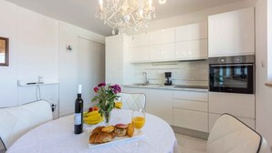 A modern kitchen with white cabinetry, a built-in oven, and a chandelier.