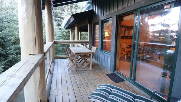A wooden deck with a table and chairs, a cushioned bench, and a large window with a view of indoor seating. - Ski Bike in out 4 bdrm, 4 bth home w pool table & media room, plus 2 sofa beds (Whistler)