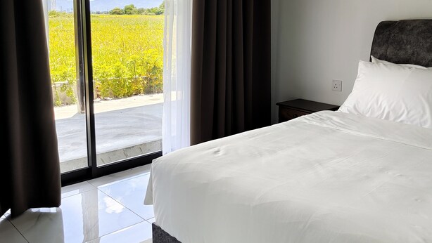 A hotel room with a bed, a nightstand, and a view of a field through a large window. - Paddy Villea Inn (Bukit Mertajam)