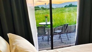 A bed with white bedding and a view of a patio with a table and chairs. - Paddy Villea Inn (Bukit Mertajam)