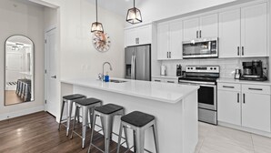 A modern kitchen with white cabinetry, stainless steel appliances, and a central island with bar stools. - Modern & Cozy Condo w/Hot Tub! (Sun Peaks)