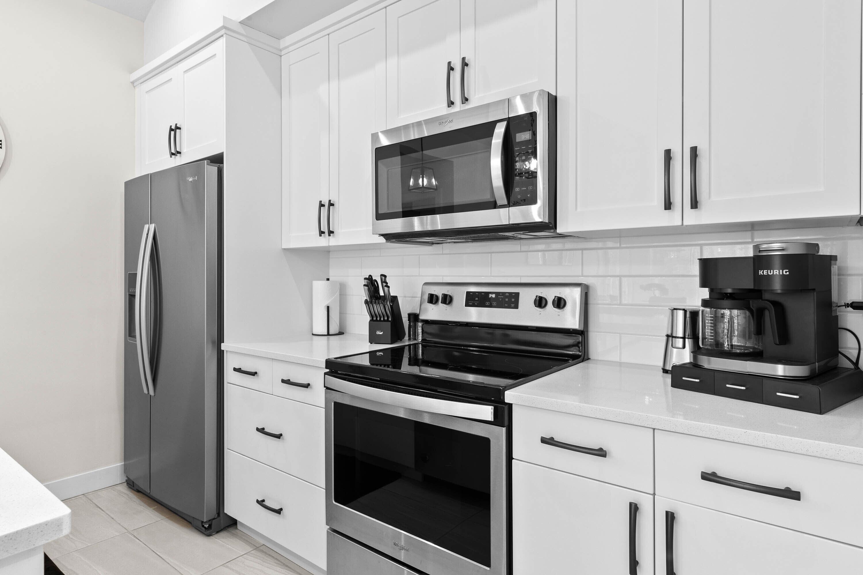 A modern kitchen with stainless steel appliances, white cabinetry, and a coffee maker.