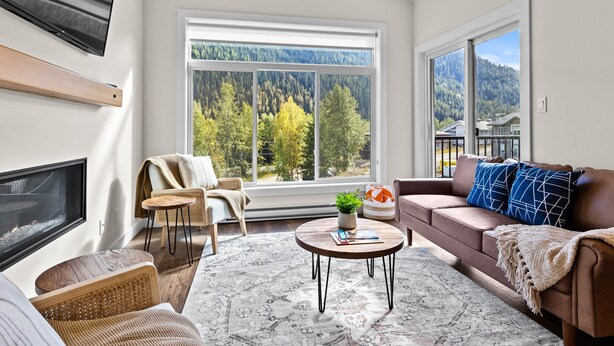 A modern living room with a fireplace, large windows, a sofa, and a coffee table. - Modern & Cozy Condo w/Hot Tub! (Sun Peaks)