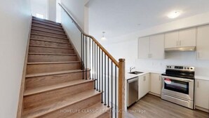 A staircase with wooden steps and black railings leading to a kitchen area with white cabinets and a stainless steel oven. - Your vacation home @Bradford, ON (Bradford West Gwillimbury)