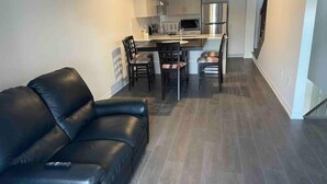 A modern kitchen with stainless steel appliances, a dining area with a black leather sofa, and a staircase leading to an upper floor. - Your vacation home @Bradford, ON (Bradford West Gwillimbury)