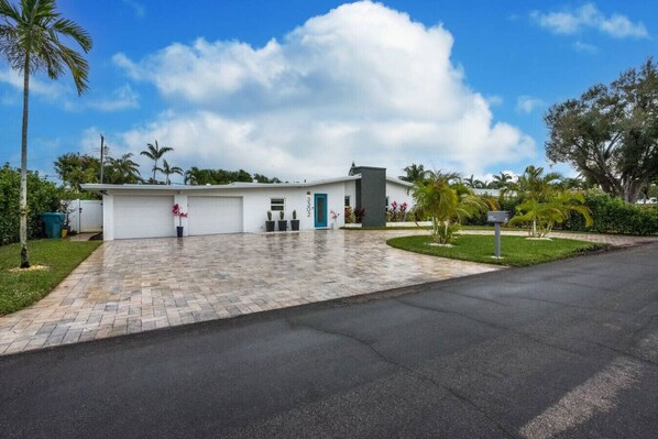 A modern building with a paved driveway, a garage, and a well-maintained lawn with palm trees.