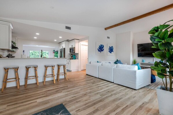 A modern kitchen with white cabinets, a central island with stools, and a dining area with a white sofa and blue cushions. - Turquoise 4BR/3BA Heated Pool Home (Boynton Beach)