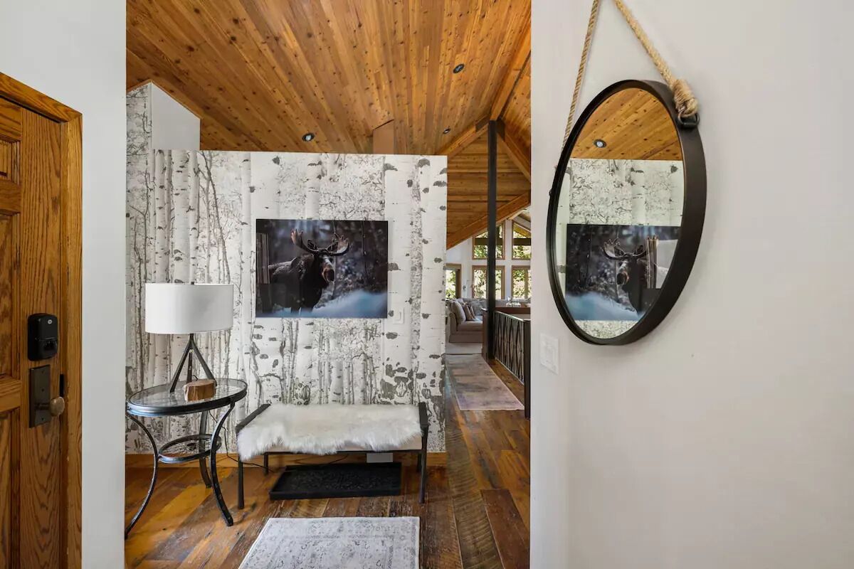 A cozy interior with a wooden ceiling, a bench, a table with a lamp, and a wall-mounted mirror.