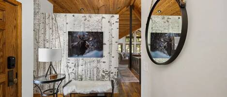 A cozy interior with a wooden ceiling, a bench, a table with a lamp, and a wall-mounted mirror.