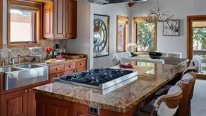 Una cocina moderna con encimeras de granito, electrodomésticos de acero inoxidable, armarios de madera y una isla grande con asientos.