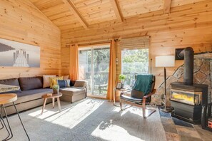 A cozy cabin interior with a stone fireplace, wooden walls, a sofa, and a dining area. - Alpine Escape Monthly Rental (Stateline)