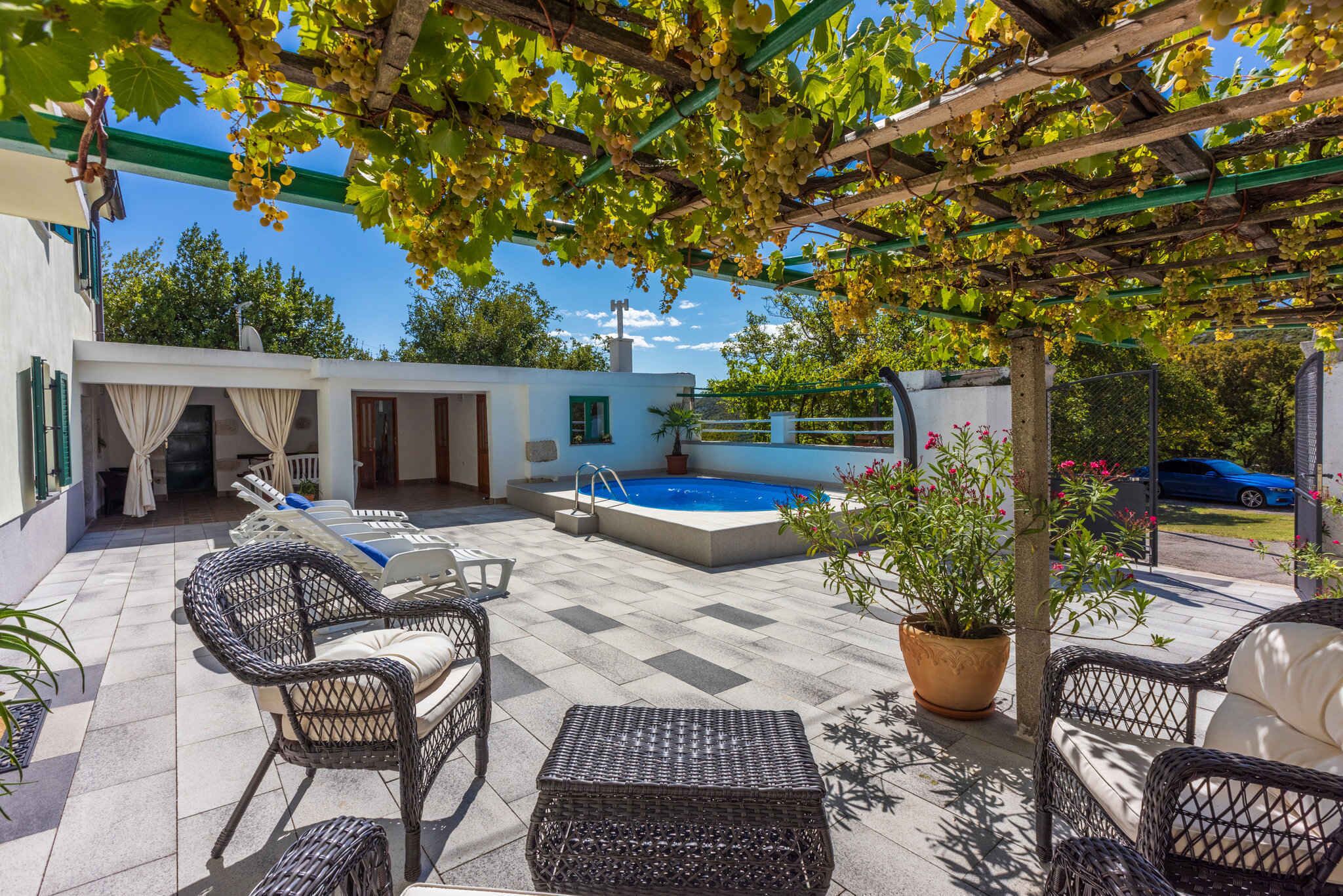 Un espace extérieur abrité, aménagé avec des meubles en osier, une piscine et une pergola couverte de plantes grimpantes.