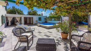 A covered outdoor area with wicker furniture, a swimming pool, and a pergola with vines.
