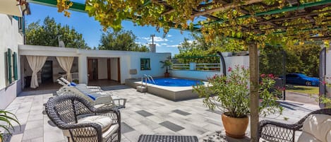 A covered outdoor area with wicker furniture, a swimming pool, and a pergola with vines.