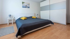 A bedroom with a bed, a nightstand, a lamp, a wardrobe, and a painting on the wall.