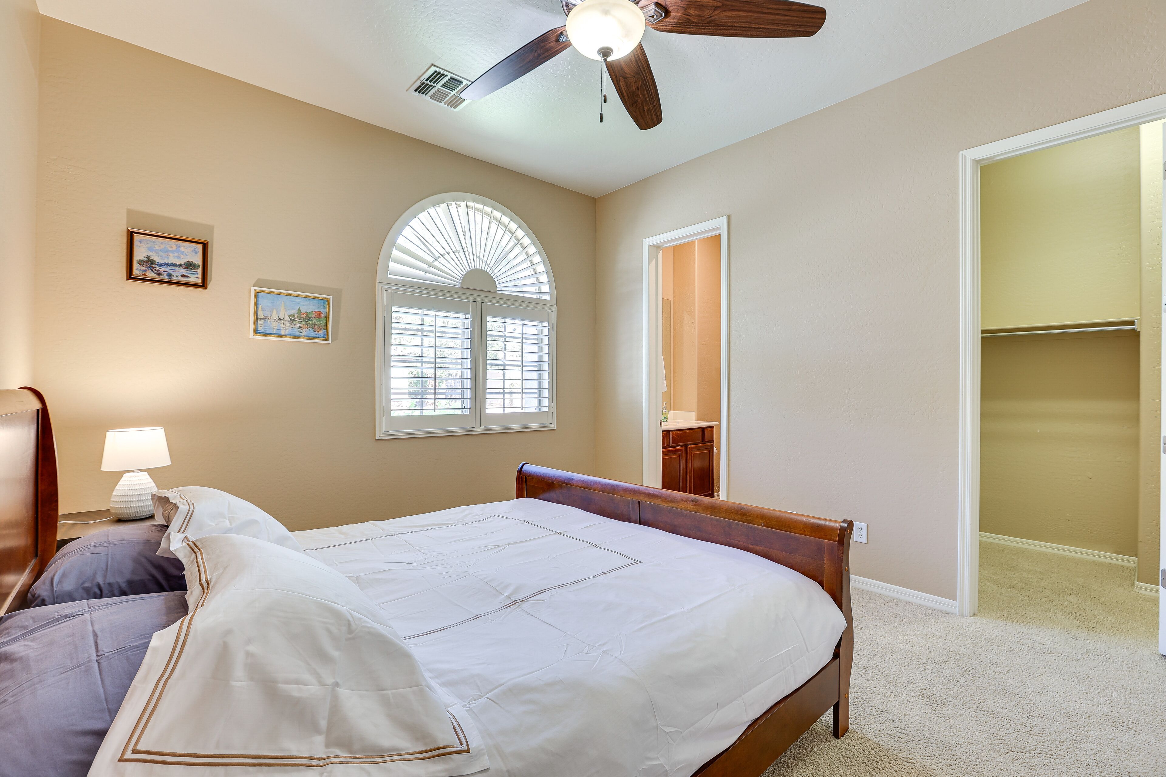 A bedroom with a bed, a ceiling fan, a window with blinds, and a door leading to another room.