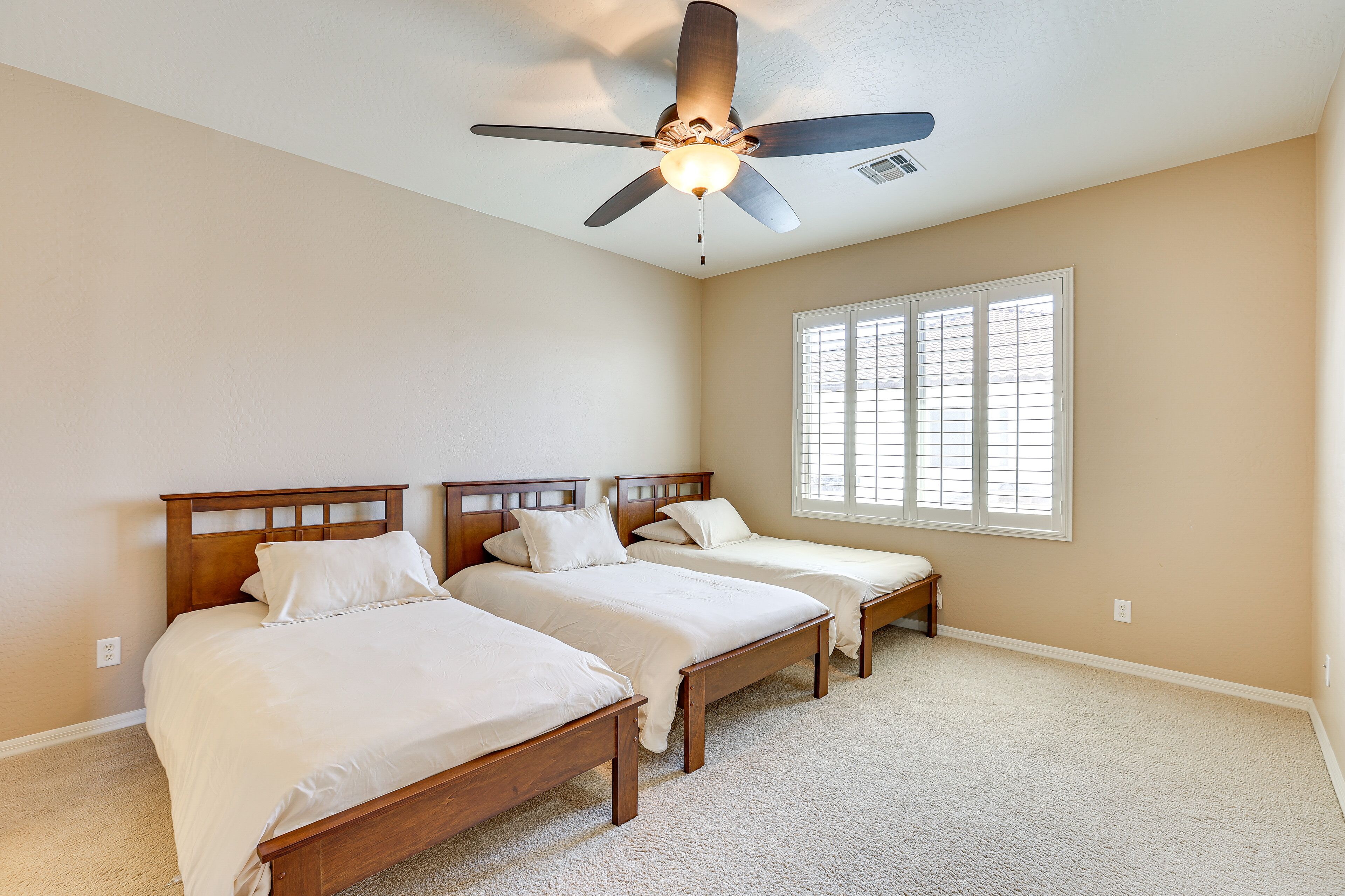 Une chambre avec deux lits simples, un ventilateur de plafond et une grande fenêtre avec des stores.